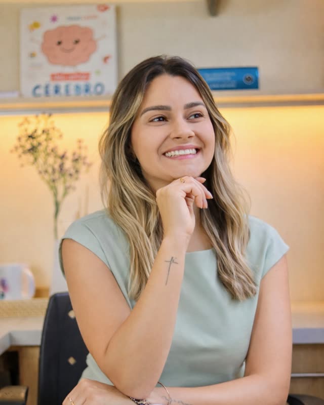 Katia Fernanda Viana no consultório, com a estante de materiais de avaliação ao fundo